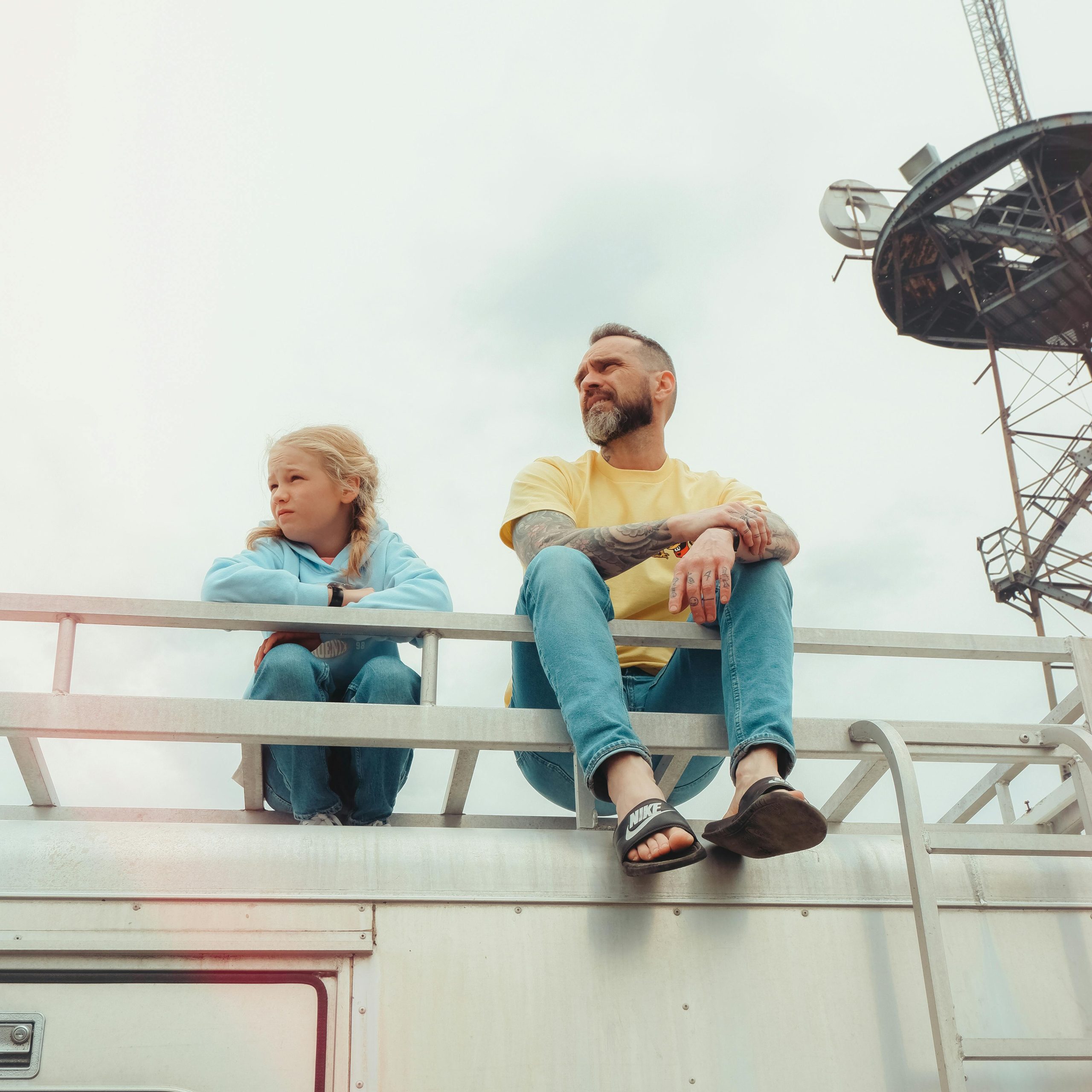 A father and daughter sit together on a rooftop, enjoying a peaceful outdoor moment.